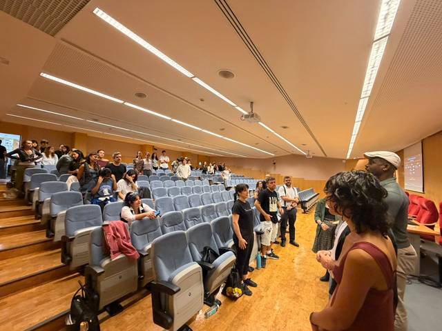 Un grupo de personas está de pie en un auditorio con asientos vacíos mirando hacia el frente.