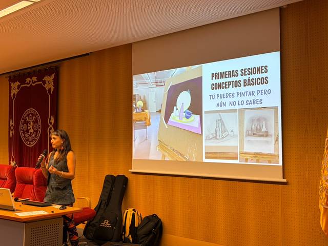 Una mujer presenta conceptos básicos de pintura mientras se proyecta una imagen en una pantalla.