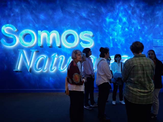 Un grupo de personas conversa frente a un fondo iluminado que dice 'Somos Naturaleza'.