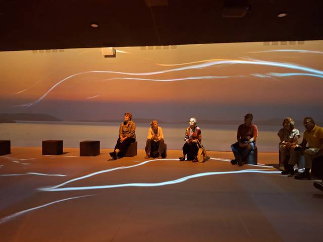Grupo de personas sentadas en un espacio con proyecciones de luz que imitan un atardecer en el fondo.