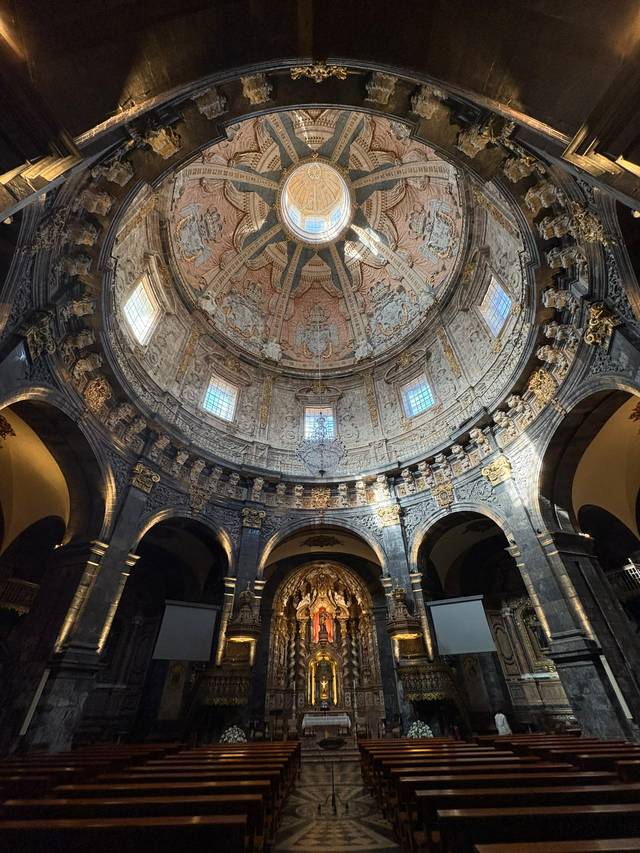 Interior de una iglesia con una magnífica cúpula decorada y bancos de madera en el pasillo.