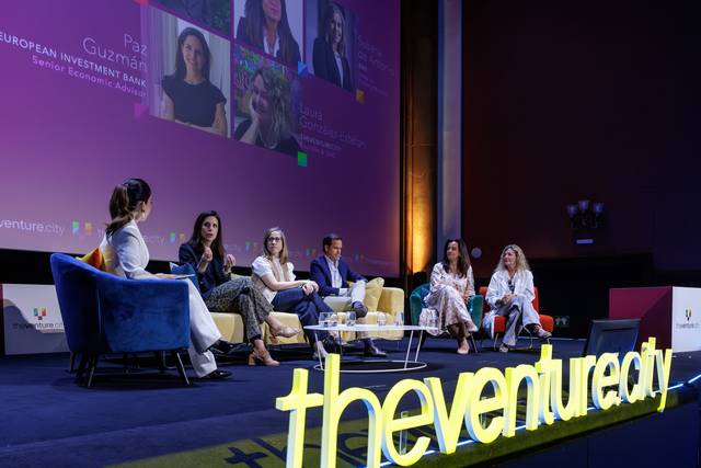 Un panel de discusión en un evento con varias panelistas sentadas en un escenario iluminado.