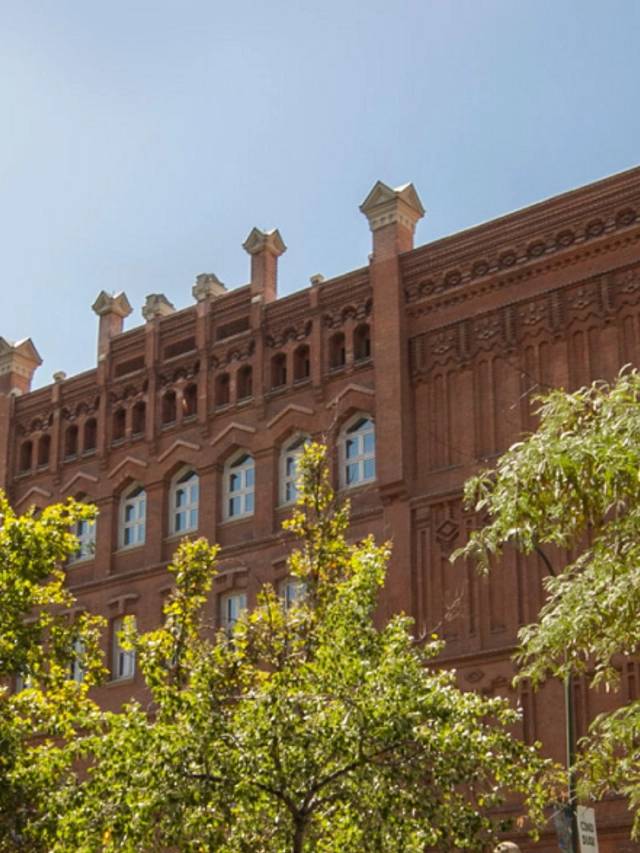 Edificio de ladrillo rojo con detalles arquitectónicos y árboles en primer plano.