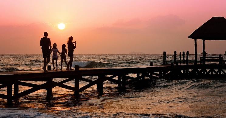 Una familia pasea por un muelle al atardecer, con el sol poniéndose en el horizonte.