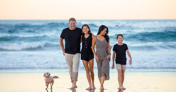 Una familia camina por la orilla de la playa al atardecer acompañada de un perro.