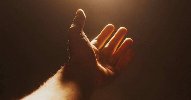 Una mano extendida hacia la luz en un ambiente suave y oscuro.