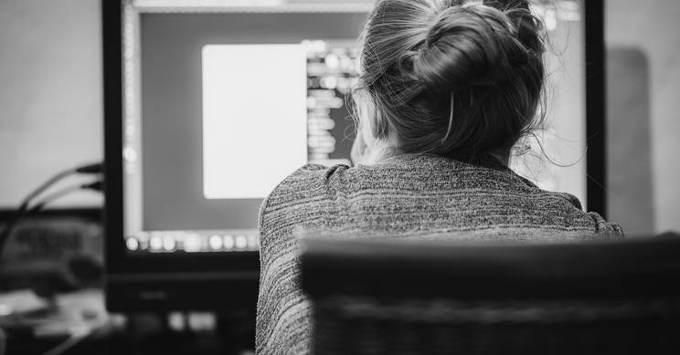 Una persona de espaldas trabaja en un ordenador, con una pantalla brillante frente a ella.
