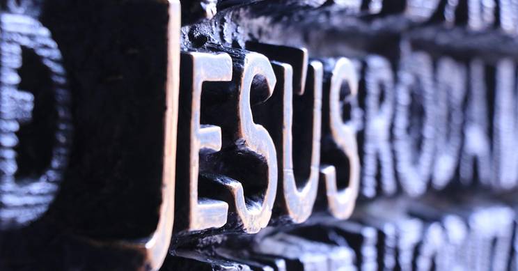 Imagen en primer plano de la palabra 'Jesús' tallada en un material oscuro.