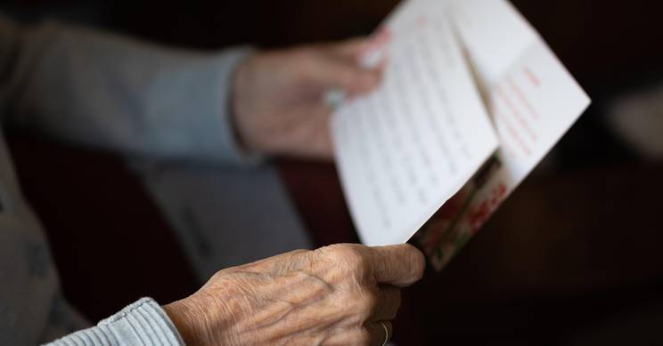 Una persona mayor sostiene una carta con ambas manos mientras la lee.