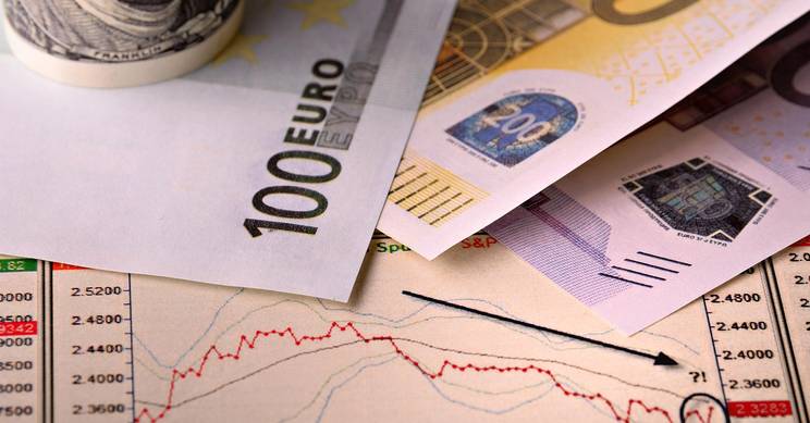 La imagen muestra billetes de euro y un gráfico financiero que indica una tendencia a la baja.