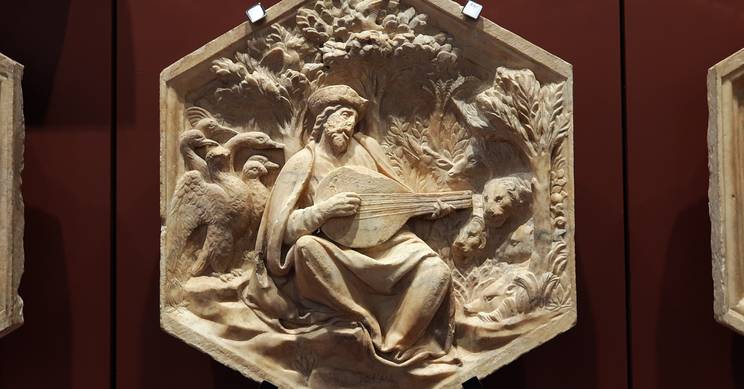 Un relieve en madera que representa a un hombre tocando laúd rodeado de naturaleza.