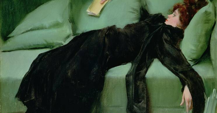 Una mujer vestida de negro se encuentra recostada en un sofá verde con un libro en la mano.