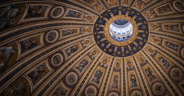 La imagen muestra el impresionante techo circular de una cúpula con ornamentos dorados y frescos.
