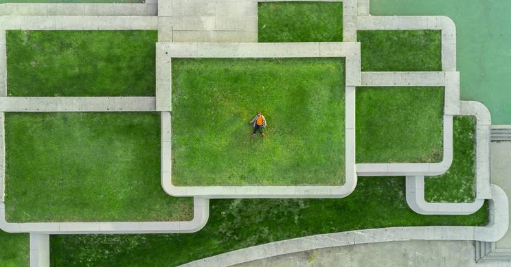 Un hombre se encuentra en un entorno urbano con césped y estructuras de concreto dispuestas de manera geométrica.