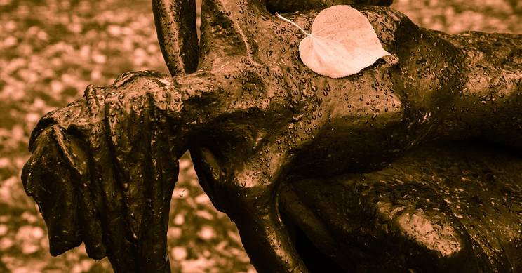 Una escultura de metal con una hoja sobre ella, rodeada de un ambiente otoñal.