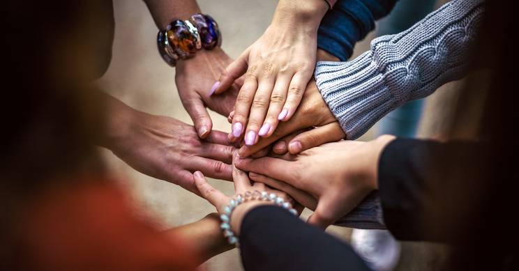 Un grupo de manos se juntan en el centro, simbolizando unión y colaboración.