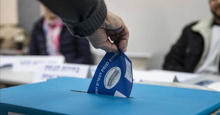 Una persona está votando al introducir una boleta en una urna electoral.