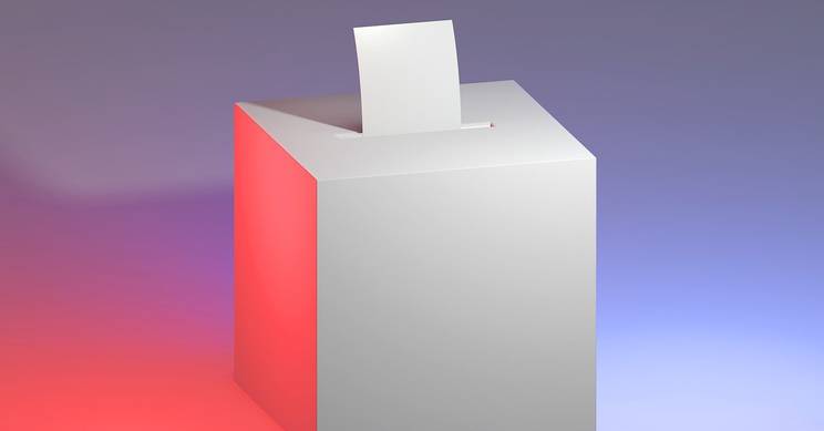 Una urna electoral blanca con una boleta en su interior sobre un fondo de luces de colores.