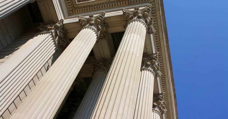 La imagen muestra columnas clásicas de un edificio bajo un cielo azul claro.