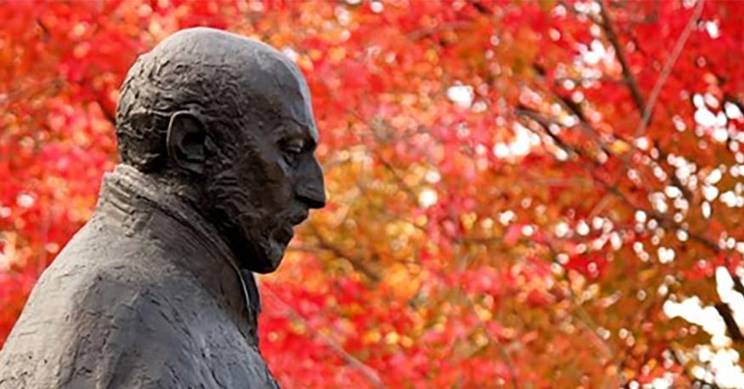 Una escultura de perfil rodeada de hojas de otoño en colores rojos.
