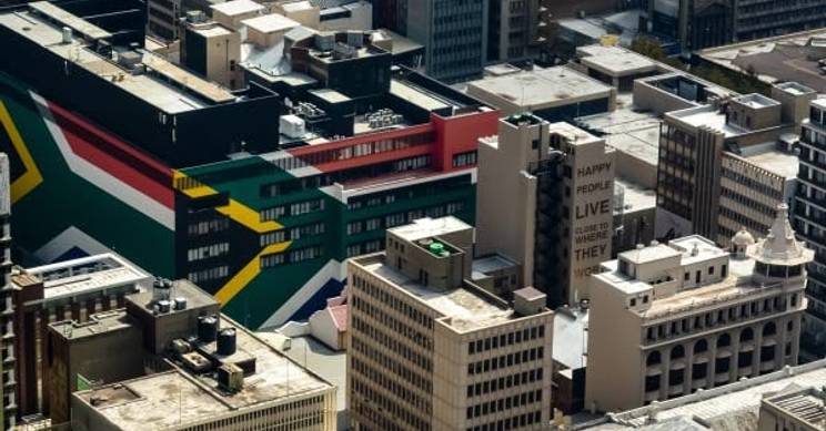 Vista aérea de un paisaje urbano con edificios y un mural colorido que muestra la bandera de Sudáfrica.