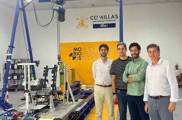 Four men standing in a laboratory with advanced mechanical equipment and a banner that reads 'Comillas ICAI'.