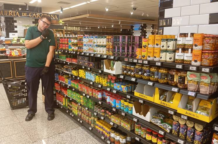 Una persona en un supermercado observa una estantería llena de productos enlatados.