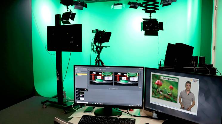 A modern television studio setup with multiple screens, cameras, and green chroma key background.