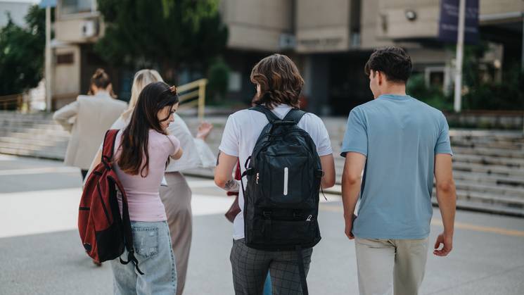Un grupo de jóvenes camina juntos hacia un edificio con mochilas en la espalda.