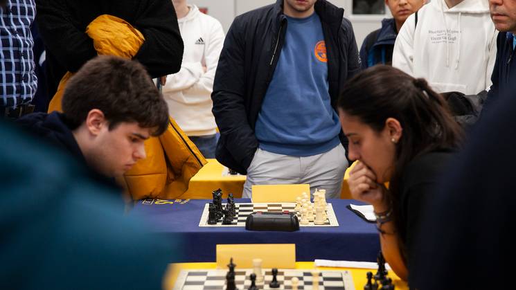 Un grupo de personas observa una partida de ajedrez entre dos jugadores concentrados.