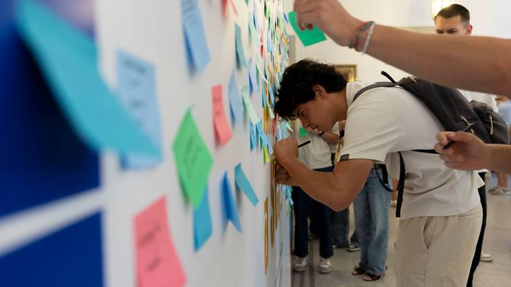 Un grupo de personas está interactuando con una pared llena de notas adhesivas de colores.