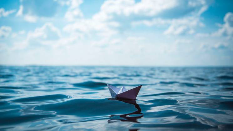 Una pequeña barca de papel navega sobre aguas tranquilas bajo un cielo despejado.
