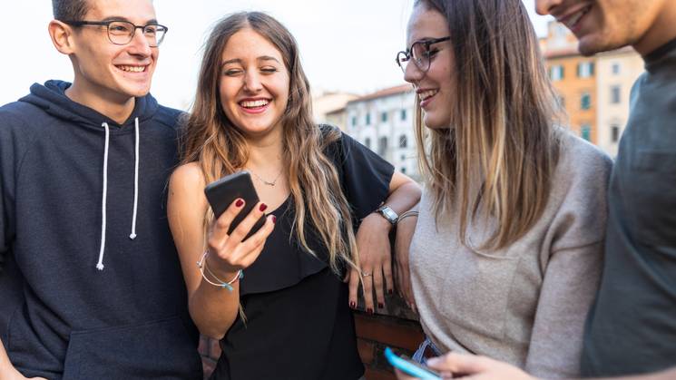 Un grupo de jóvenes sonríe mientras miran un teléfono móvil en un ambiente urbano.