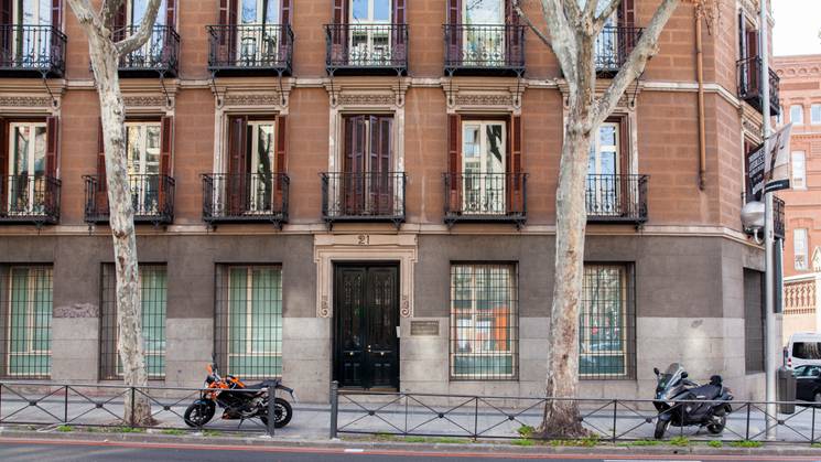 Edificio de estilo clásico con balcones, árboles y motocicletas estacionadas en la acera.