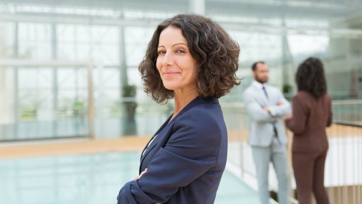 Una mujer sonriente de cabello rizado se encuentra en un entorno moderno de oficina.