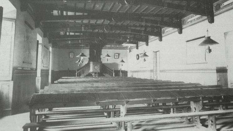 Vintage black and white photo of an empty dining hall with long tables and benches.