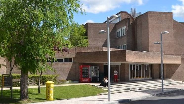 Modern brick building with a tree and walking path, featuring people sitting and walking outside.