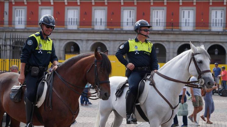 Dos policías a caballo patrullan en una plaza pública.