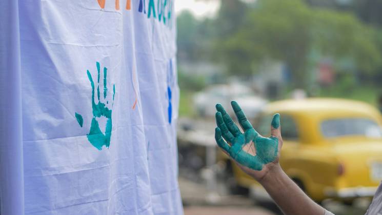 A person leaving a teal handprint on a banner at a community event.
