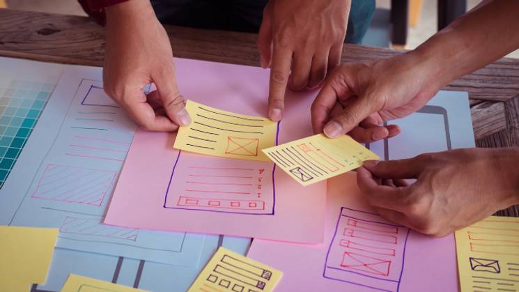 Un grupo de personas trabaja en el diseño de un prototipo con notas adhesivas en un escritorio.