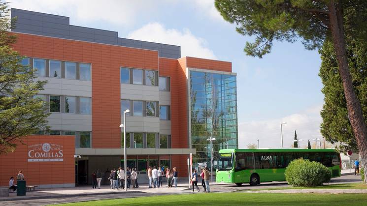 Modern university building with students walking in front and a green bus parked nearby.