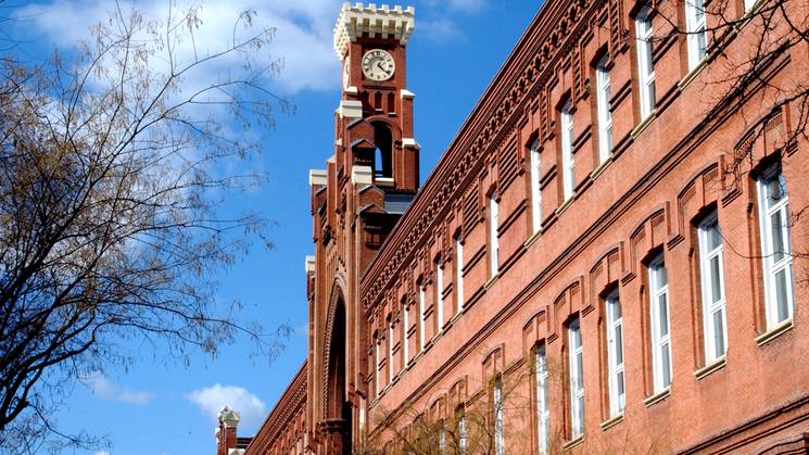 A historic brick building with a distinctive clock tower under a clear blue sky.