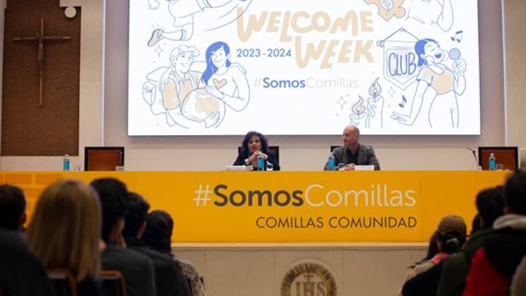 Dos personas están participando en una mesa redonda durante la Welcome Week de Comillas en un auditorio lleno de estudiantes.