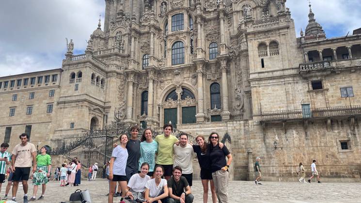 Un grupo de personas sonrientes posa frente a una impresionante fachada arquitectónica en un día nublado.