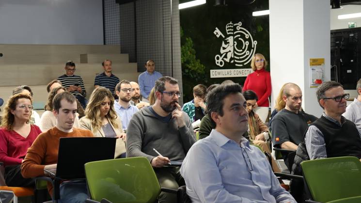 Una reunión con un grupo de personas sentadas en una sala, prestando atención a una presentación.