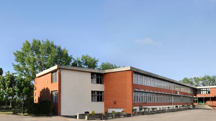 Panoramic view of a modern educational building with a spacious forecourt and surrounding greenery.