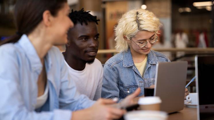 Un grupo de tres jóvenes conversando y trabajando en un café.