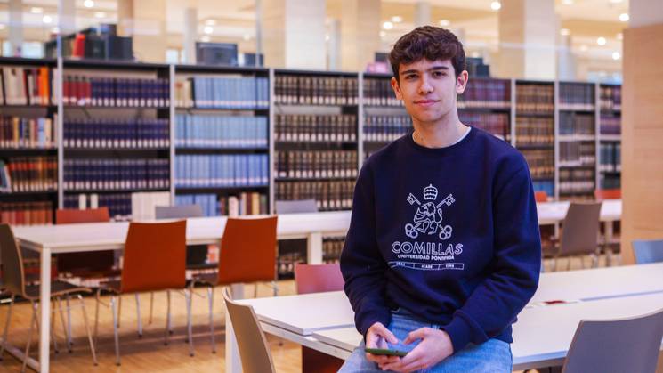 Joven estudiando en la biblioteca de la Universidad Comillas con libros y mesas de estudio.