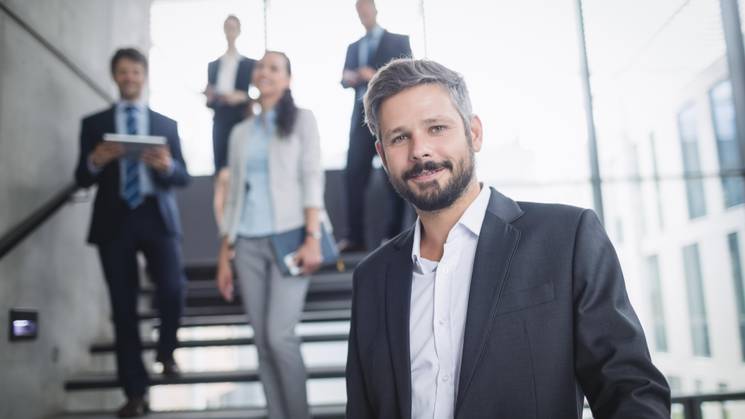 Un grupo de profesionales en un entorno de oficina moderna, con un hombre al frente sonriendo.