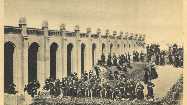 Historic black-and-white photo of people gathered at an aqueduct with colonial architecture.